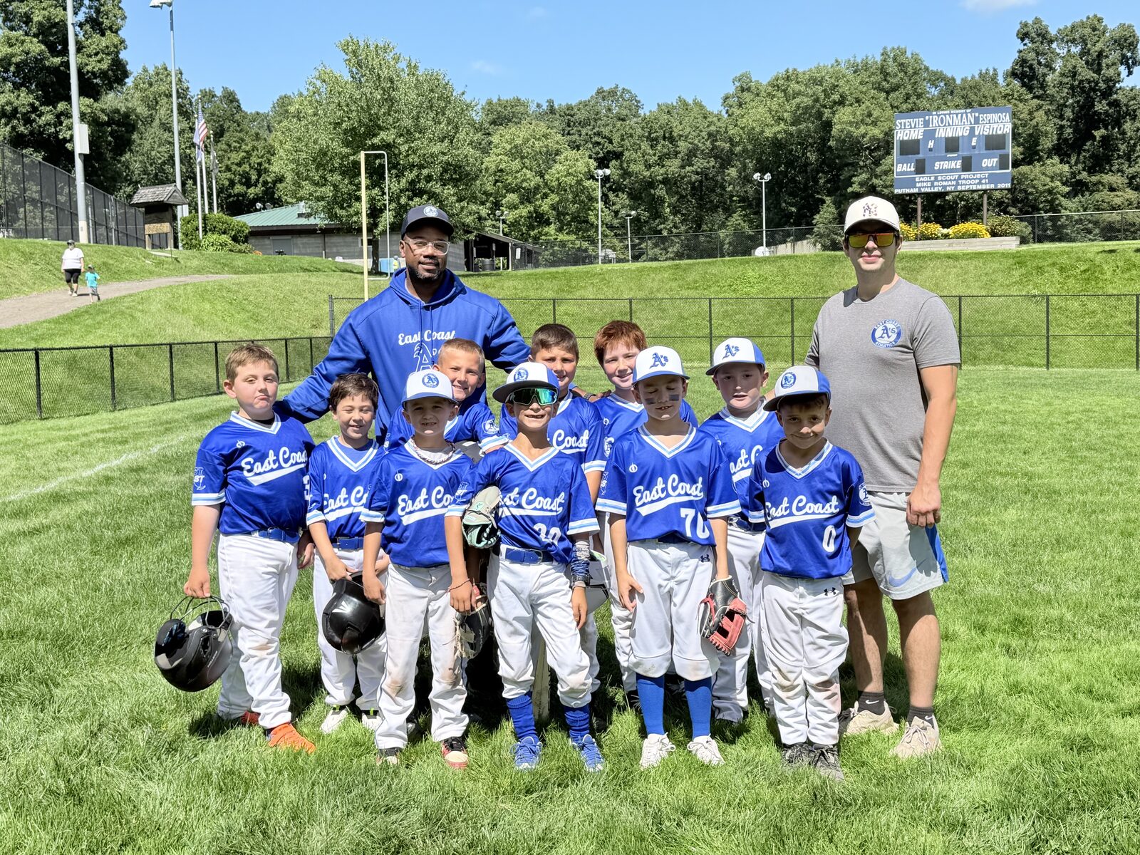 Young East Coast Athletics baseball players with their coaches in the outfield